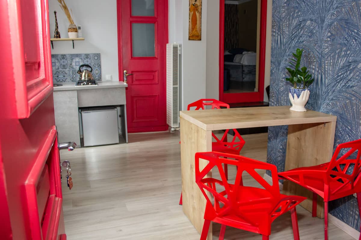 A compact kitchen with a red door, a small refrigerator, and a wooden table with red chairs.