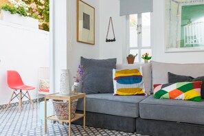 A modern living room with a grey sofa, colorful pillows, a small table with a vase, and a red chair.