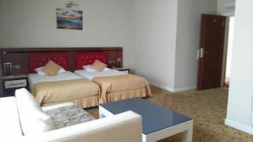 Una habitación de hotel con dos camas, una mesita, un sofá y una puerta.