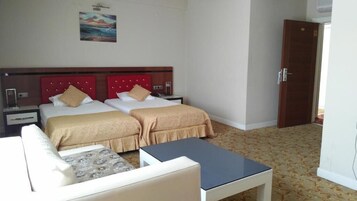 Una habitación de hotel con dos camas, una mesita, un sofá y una puerta.