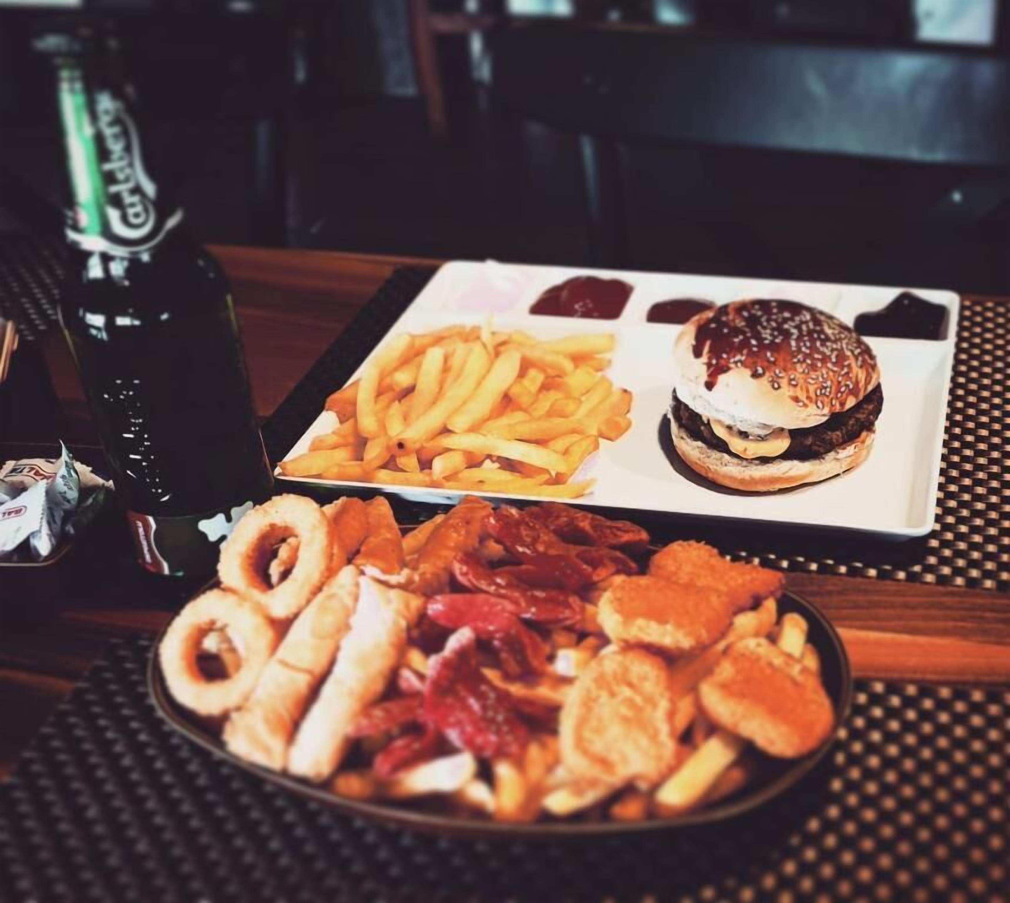 Una mesa con un plato de comida que incluye una hamburguesa, papas fritas y varios bocadillos.