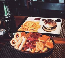 Una mesa con un plato de comida que incluye una hamburguesa, papas fritas y varios bocadillos.