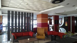 Un hall d’hôtel moderne avec un espace salon comprenant des canapés et des fauteuils, un comptoir d’accueil et un pilier décoratif.