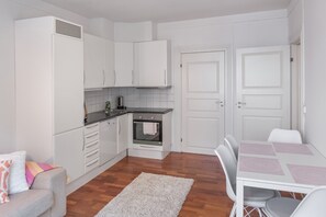 A compact kitchen with white cabinets, a built-in oven, and a dining area with a table and chairs. - Aalesund Apartments - Near Harbour (Ålesund)