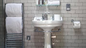 A bathroom with a white sink, glass shelves above it, and a towel rack with two towels.