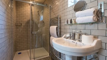 Un baño moderno con ducha de vidrio, un lavabo blanco con espejo y artículos de tocador ordenados.
