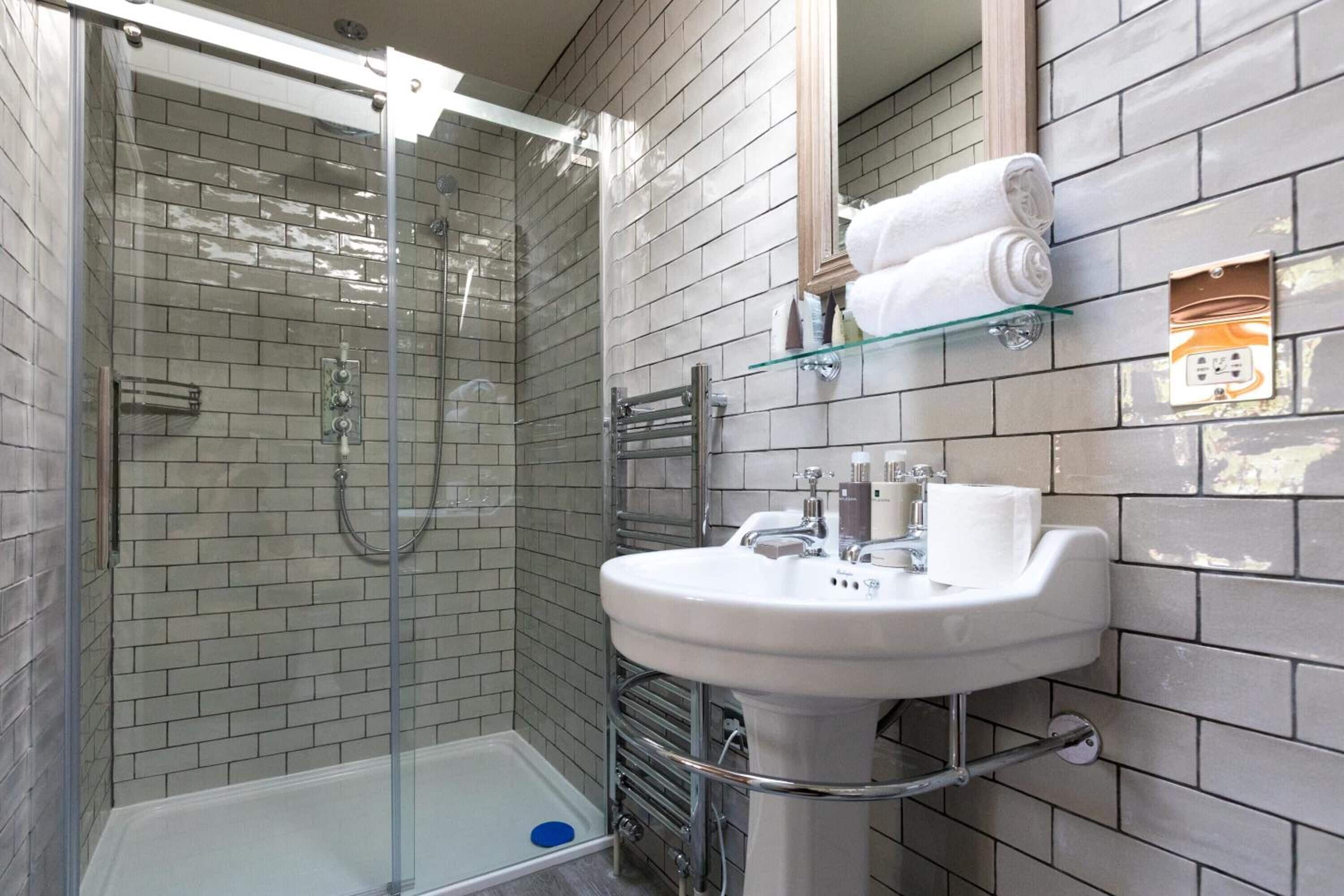 A bathroom with a glass-enclosed shower, a white sink, and a towel rack.