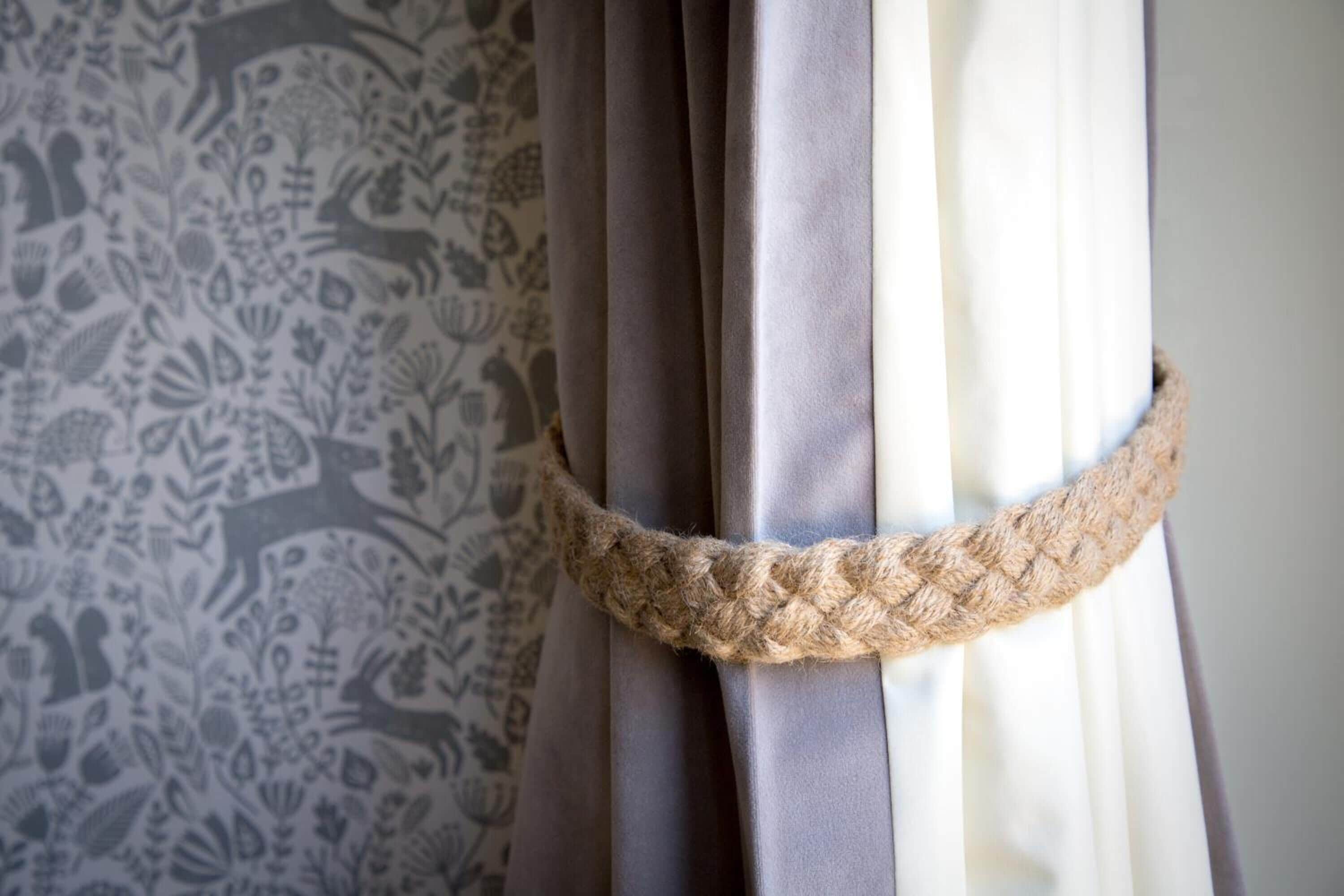 A curtain with a rope tied around it, a patterned wallpaper, and a plain wall.