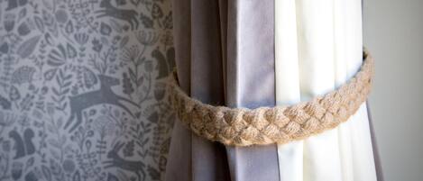 A curtain with a rope tied around it, a patterned wallpaper, and a plain wall.
