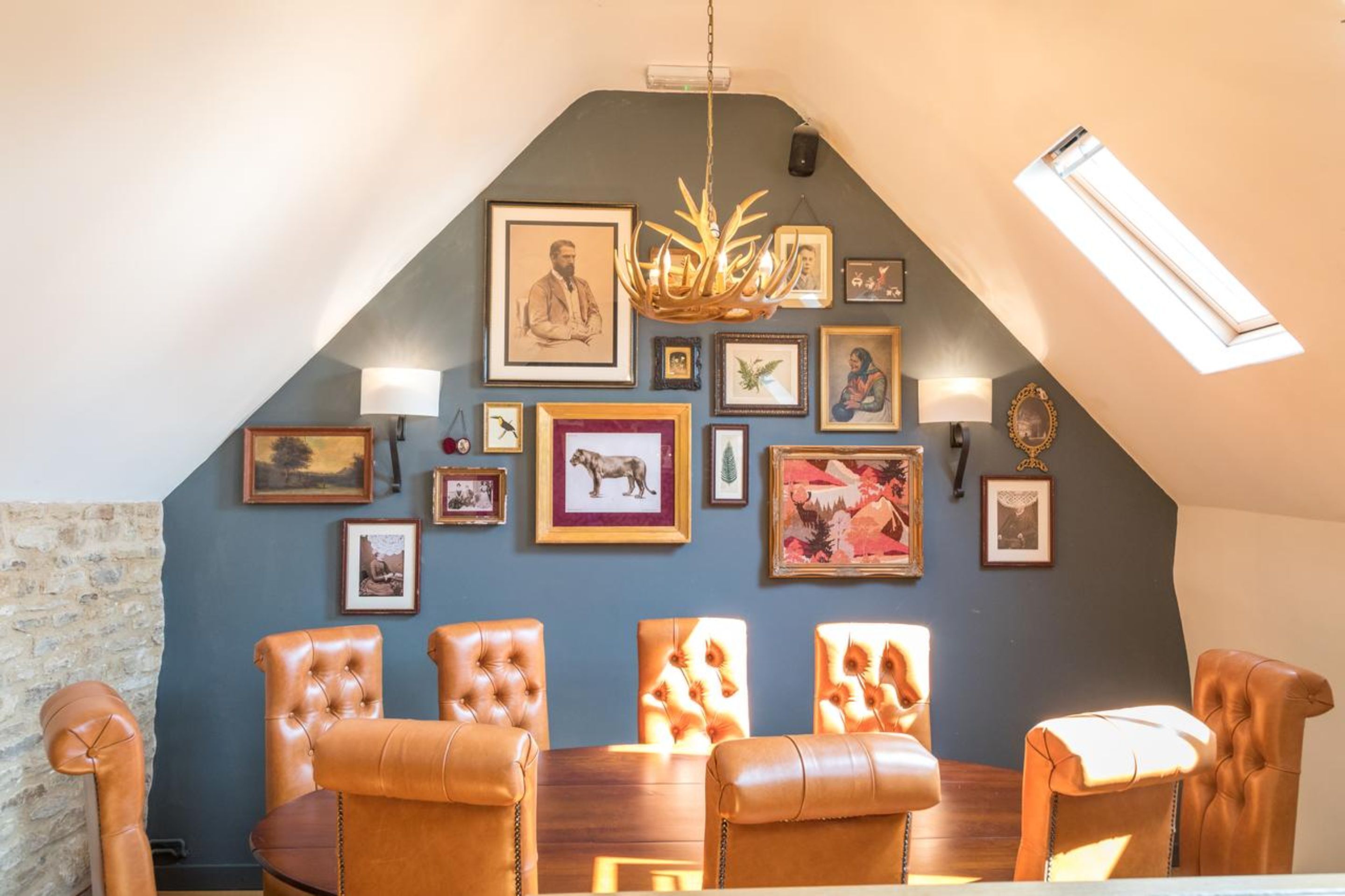 A dining area with leather chairs, a chandelier, and various framed pictures on the wall.