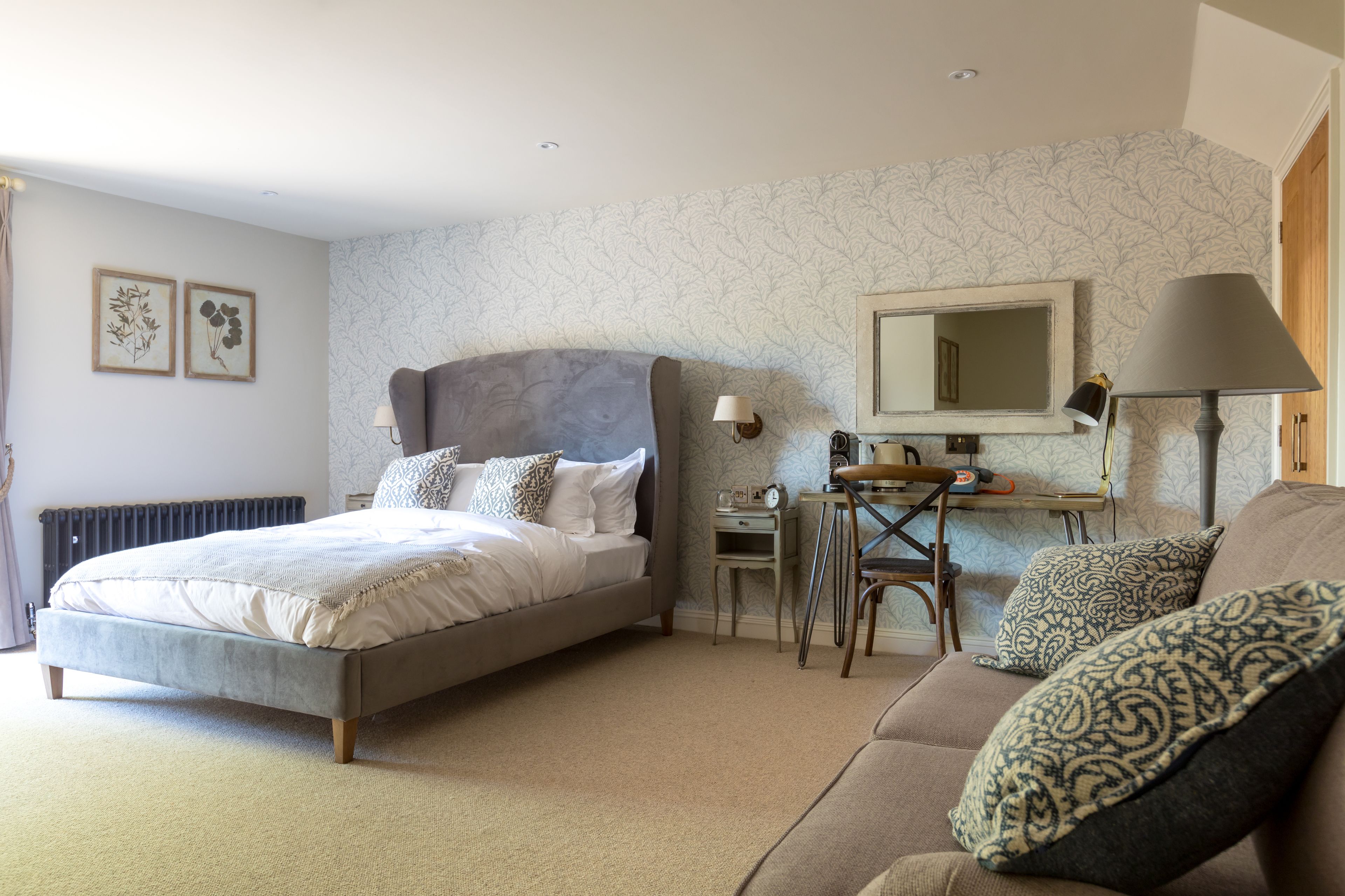 A bedroom with a bed, a desk, a chair, a sofa, and a mirror.