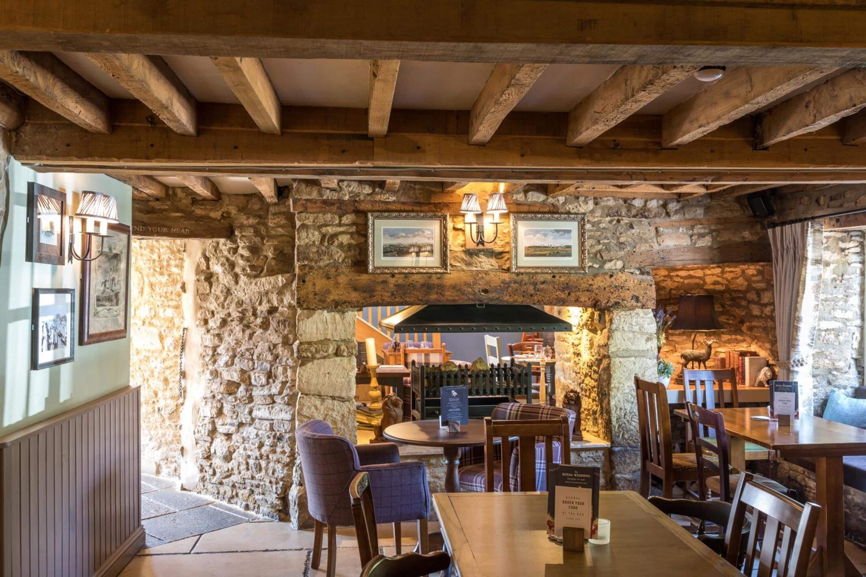 A rustic interior with stone walls, wooden beams, and tables and chairs arranged for dining.