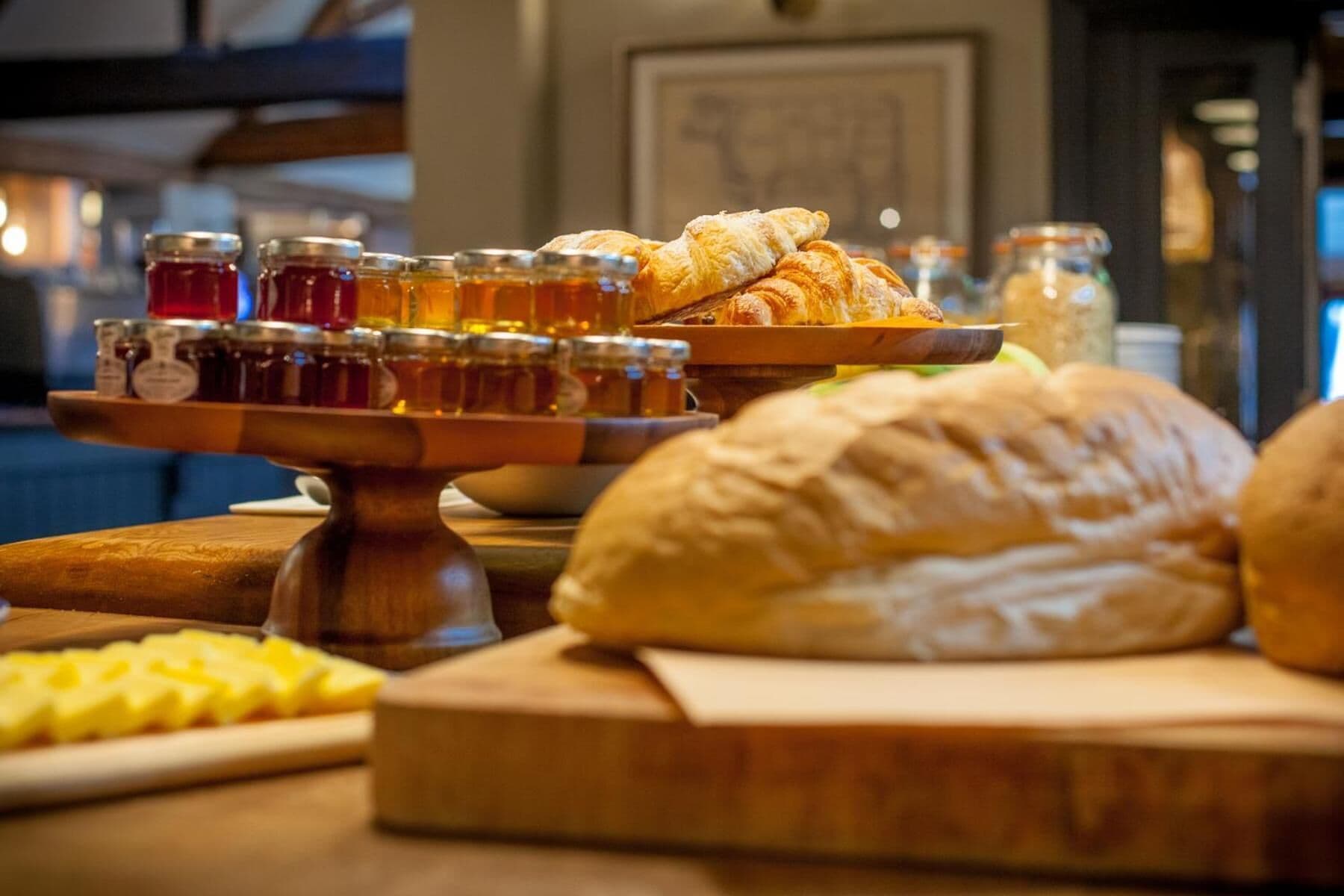 Une table sur laquelle on trouve divers aliments, notamment des pots de miel, des croissants et un pain.
