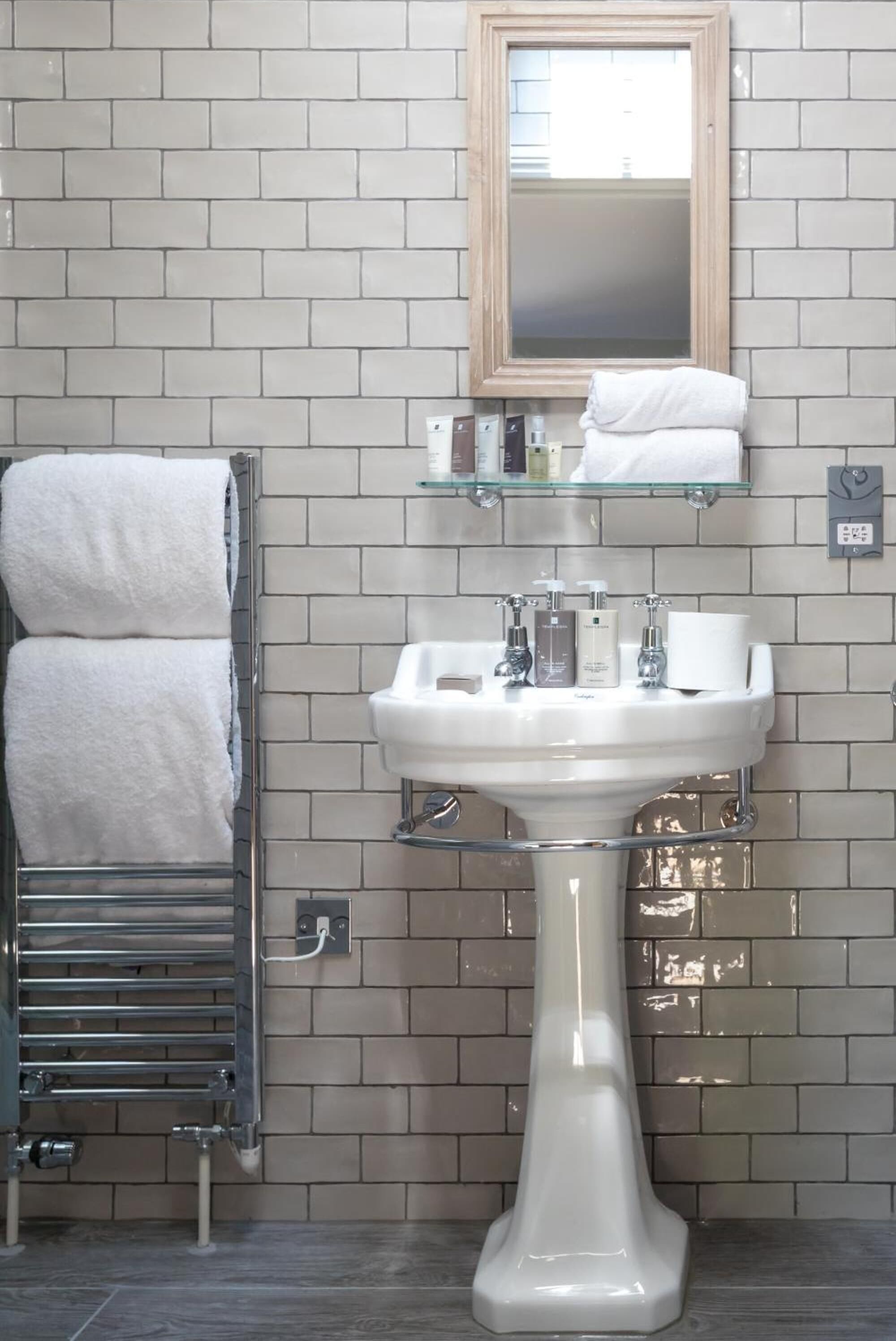 A bathroom with a white sink, a glass shelf above it, and a towel rack with two towels.