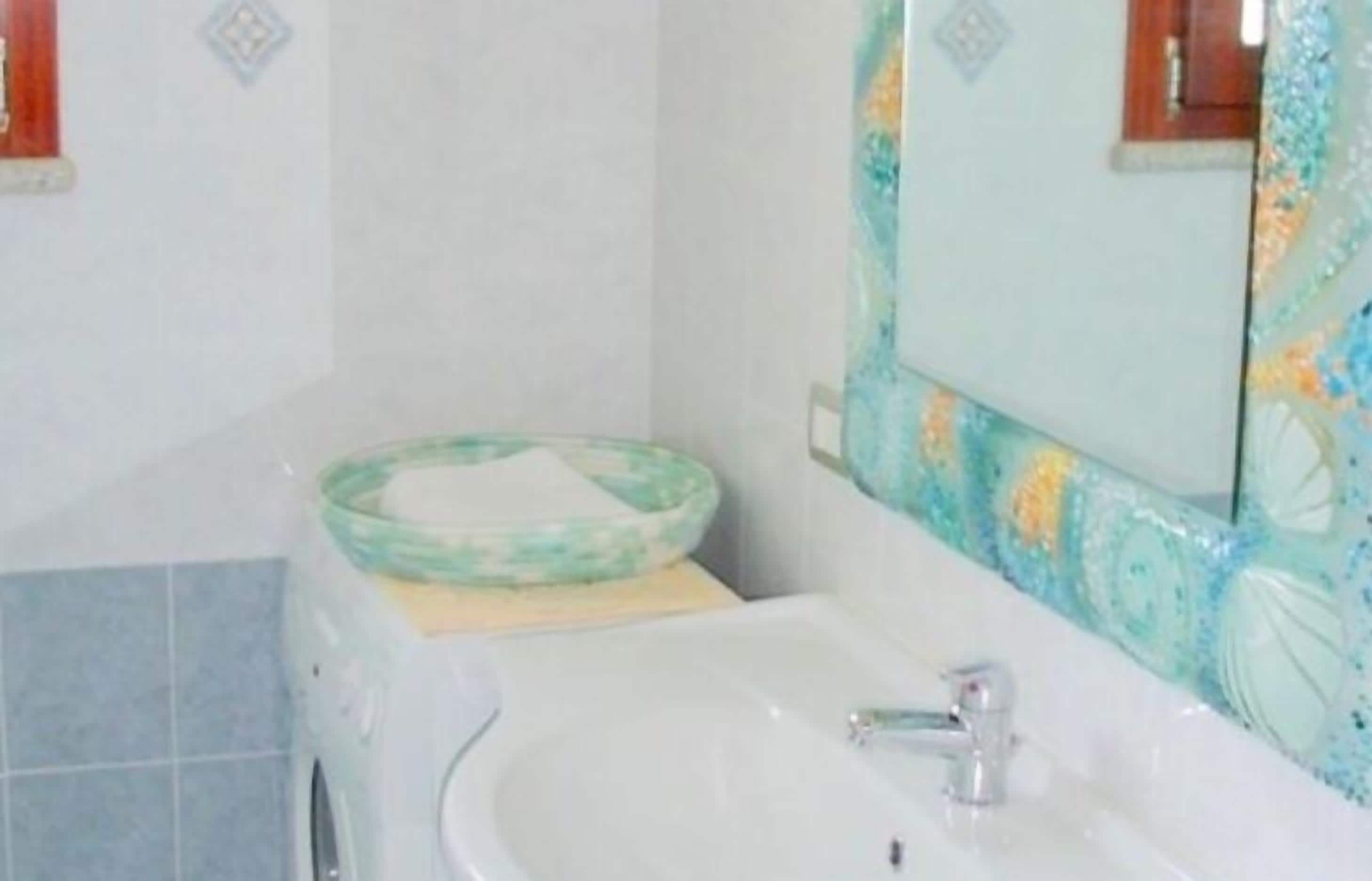 Une salle de bain avec un lavabo blanc, un receveur vert et un miroir agrémenté d’un pare-éclaboussures décoratif.