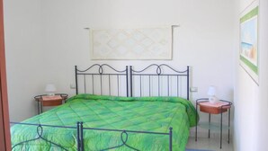 A bedroom with a bed, two bedside tables, a wall hanging, and a painting. - Villa Stella Maris (Budoni)