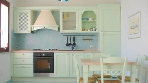 A kitchen with light green cabinets, a stove, and a dining area with a table and chairs. - Villa Stella Maris (Budoni)