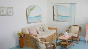 A cozy room with a sofa, two wicker chairs, a small table, and wall art depicting a beach scene. - Villa Stella Maris (Budoni)