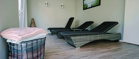 A room with a wicker lounge chair, a wicker basket with towels, and a framed picture on the wall.
