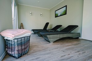 A room with a wicker lounge chair, a wicker basket with towels, and a framed picture on the wall. - Waastwinj (Utersum)