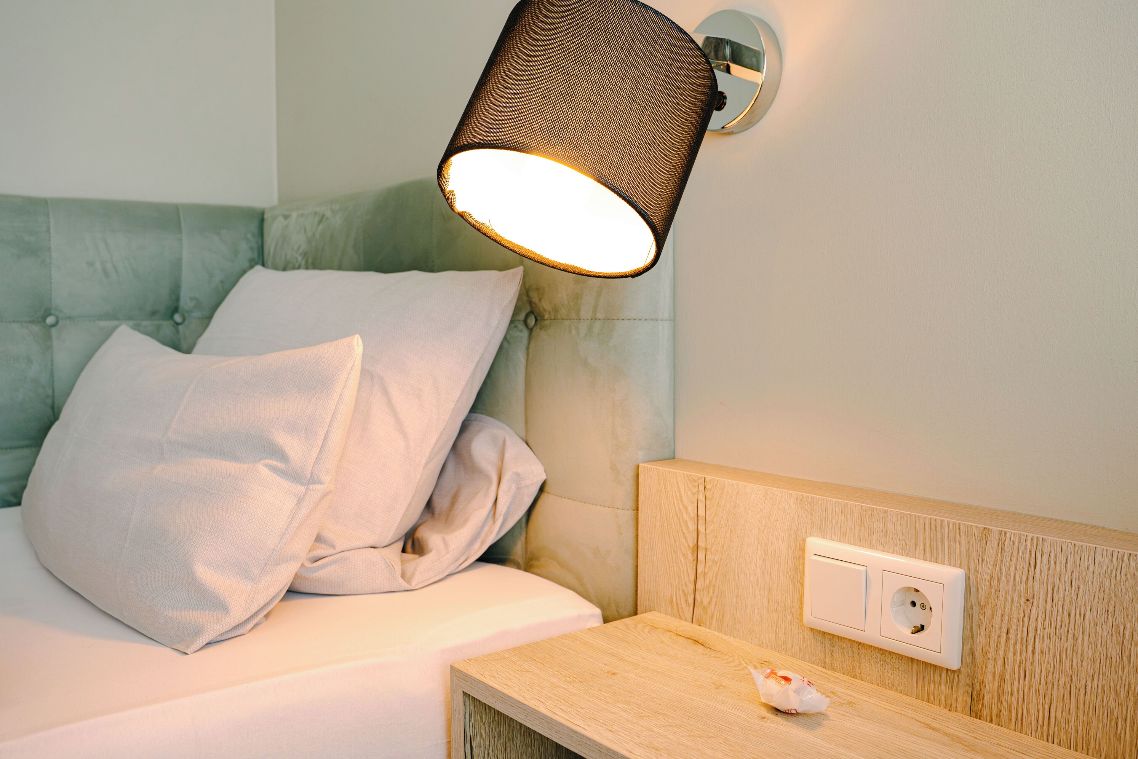 A bed with a headboard, pillows, a bedside table, and a wall-mounted lamp.