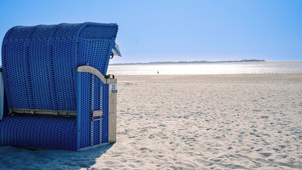 A beach chair with a number tag, a sandy beach, and a distant shoreline. - Waastwinj (Utersum)