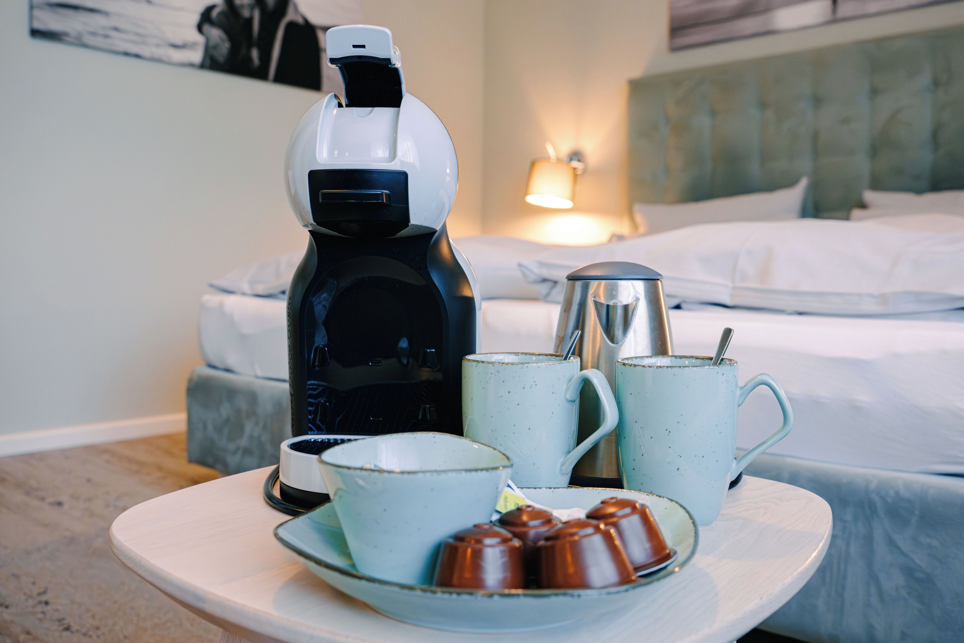 Une chambre d’hôtel avec un lit, une lampe de chevet, une machine à café et un plateau contenant une tasse, une soucoupe et une assiette de chocolats.