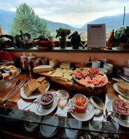 Un bufé con diversos quesos, carnes y panes, con una vista panorámica a las montañas de fondo.