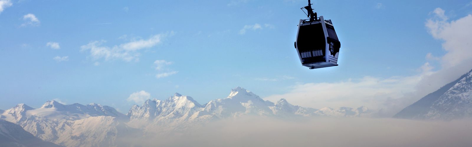 A cable car suspended above a mountainous landscape with snow-covered peaks and a clear sky.