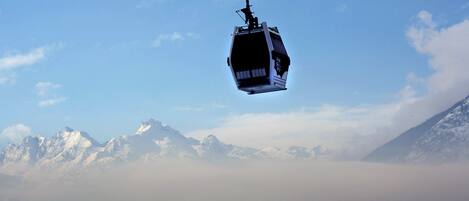 A cable car suspended above a mountainous landscape with snow-covered peaks and a clear sky.