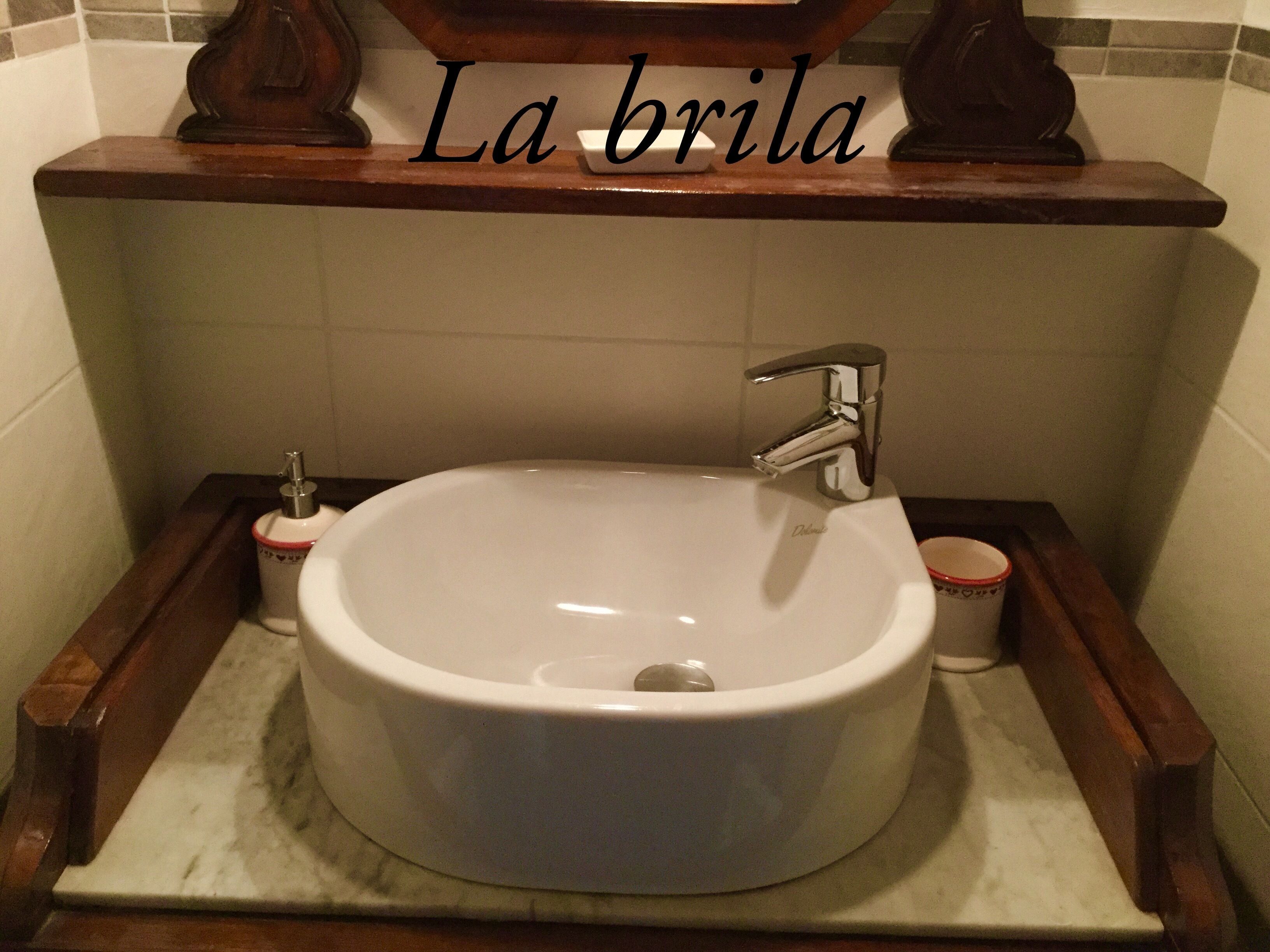 Un baño con un lavamanos blanco, un grifo cromado y un dispensador de jabón. La pared tiene un salpicadero de azulejos y una repisa sobre el lavamanos con un adorno.