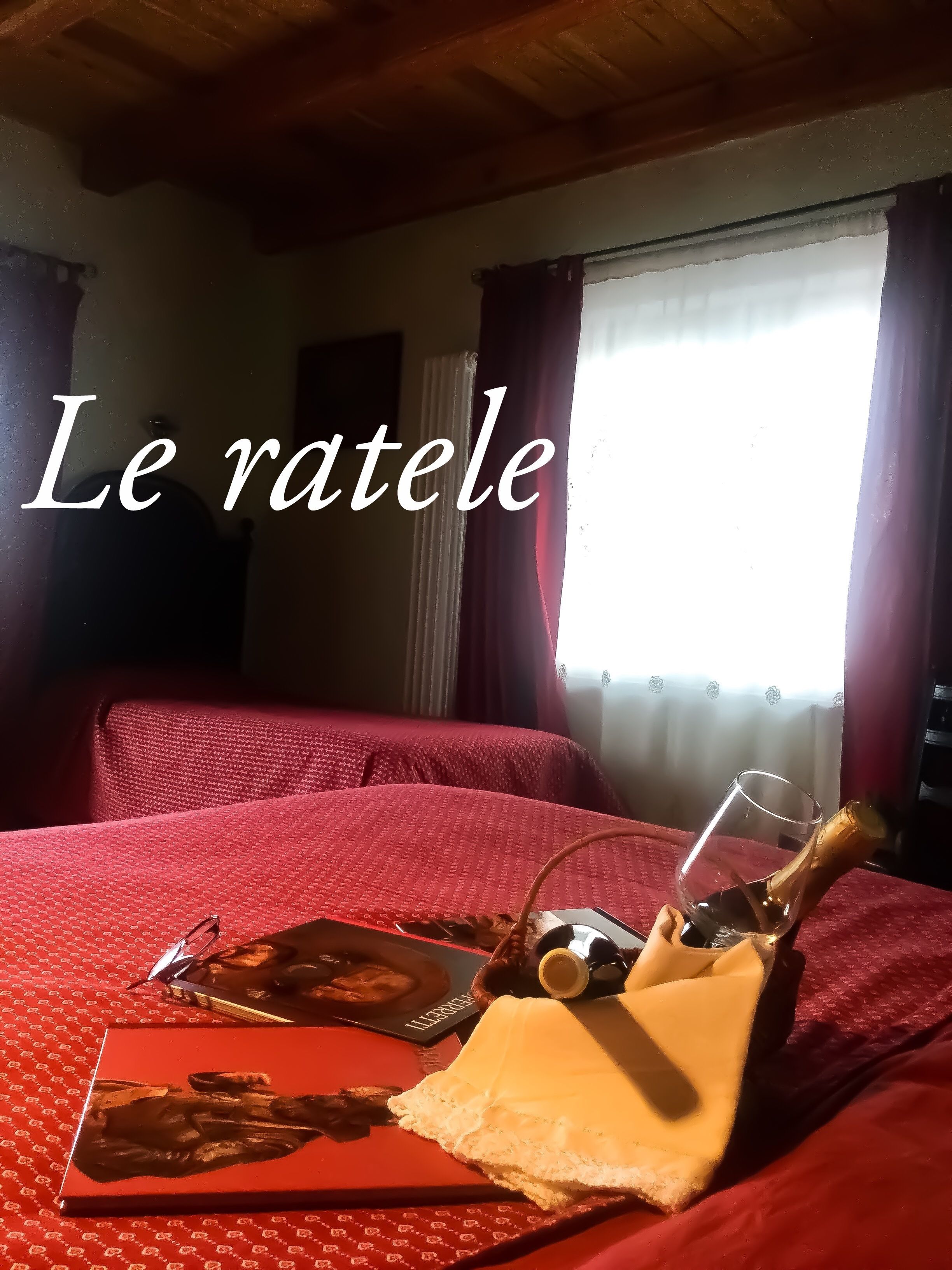 Una habitación de hotel con una cama, un ventanal con cortinas y una mesa con una botella, vasos y un libro.