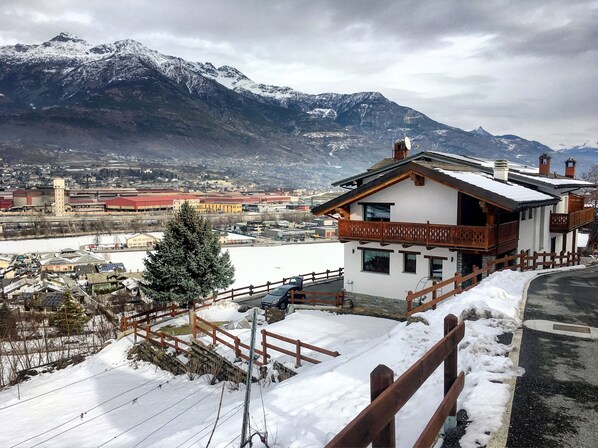 A mountain cabin with a wooden balcony, a snow-covered landscape, and a view of distant mountains. - Agriturismo Chevres a Cheval (Charvensod)
