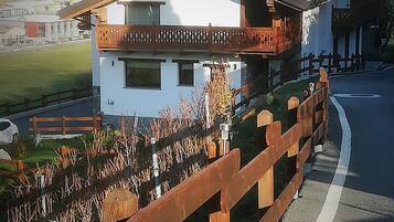 Una casa de dos pisos con balcón, cerca viva de madera y vistas del paisaje circundante.