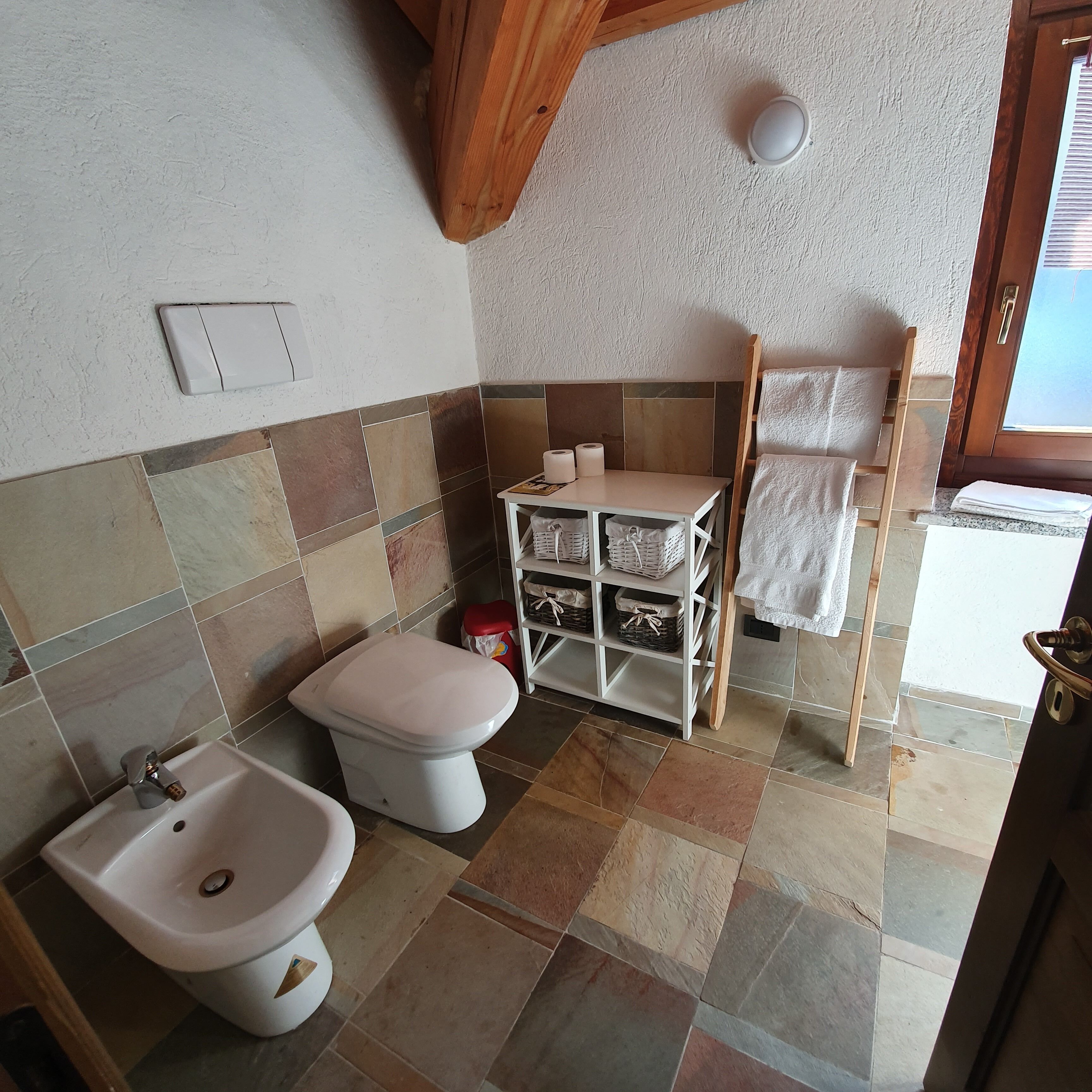A bathroom with a toilet, bidet, and shelves with towels.