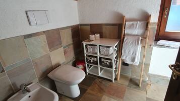 A bathroom with a toilet, bidet, and shelves with towels.