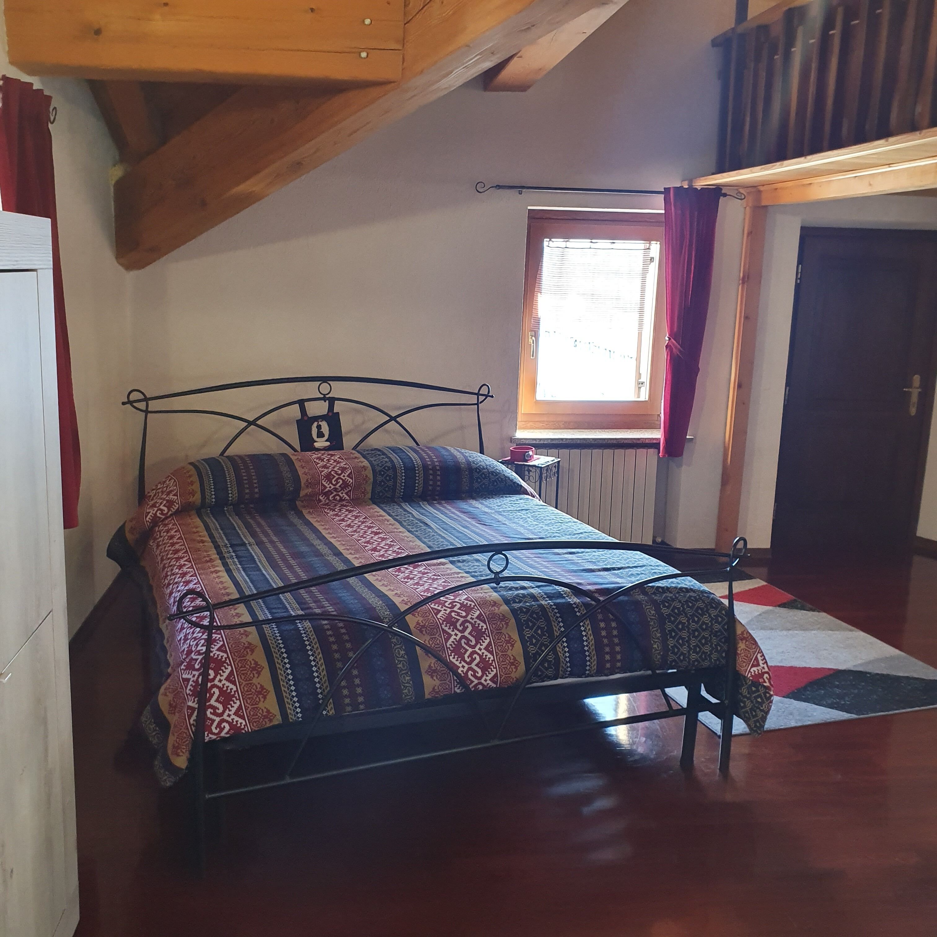 Quarto com cama, janela com cortinas, radiador e porta.