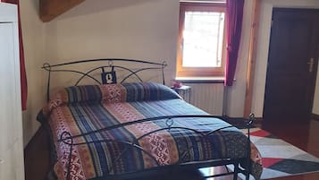 Una camera da letto con un letto, una finestra con tende, un termosifone e una porta.