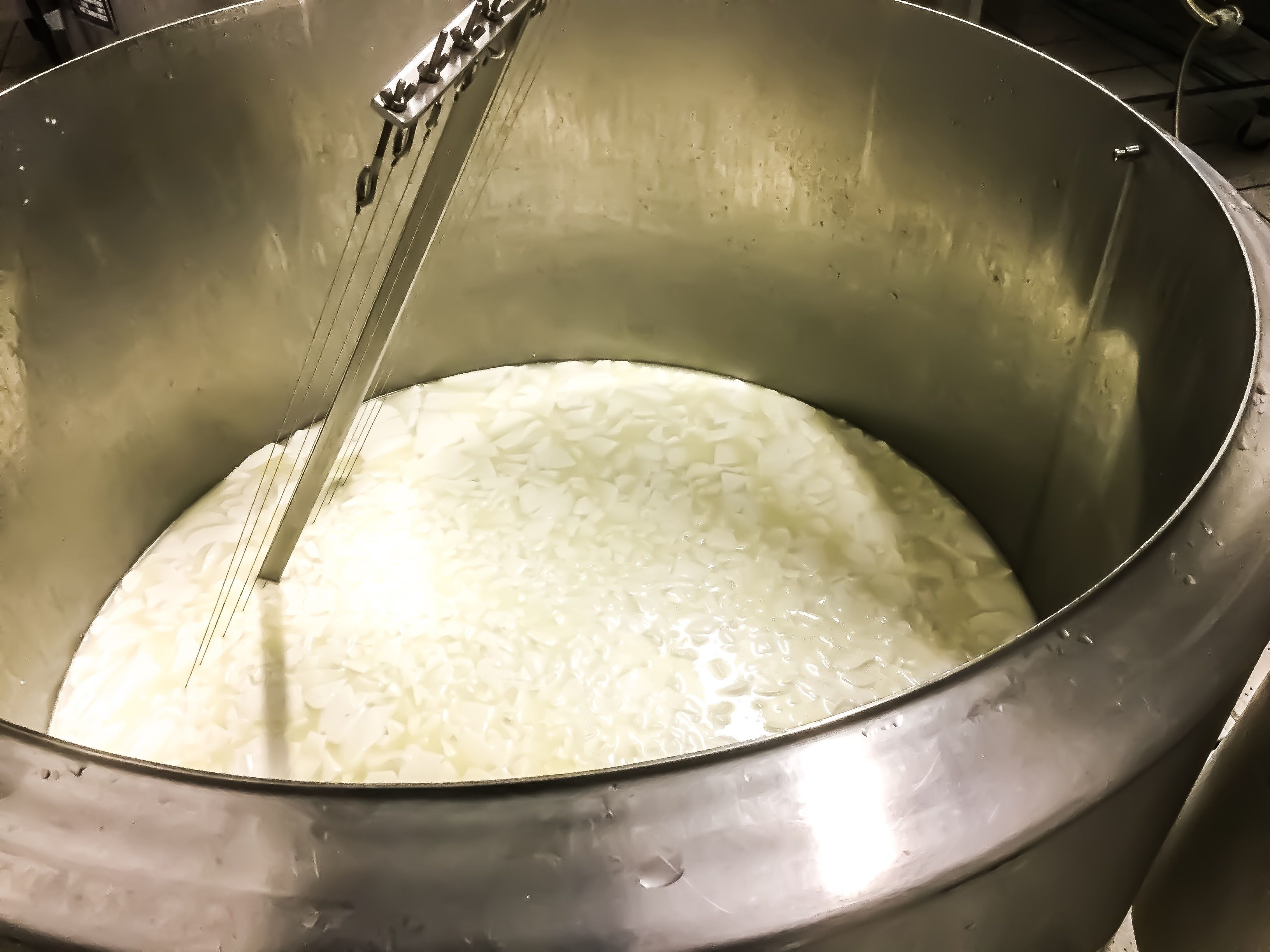 Une casserole en acier inoxydable dotée d’une anse en chaîne, contenant un liquide blanc, vraisemblablement du lait ou une substance similaire.