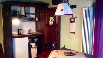 Una stanza accogliente con una panca in legno, un tavolo da pranzo con tovaglia bianca e decorazioni a forma di cuore, un angolo cottura con bollitore e un addobbo appeso.