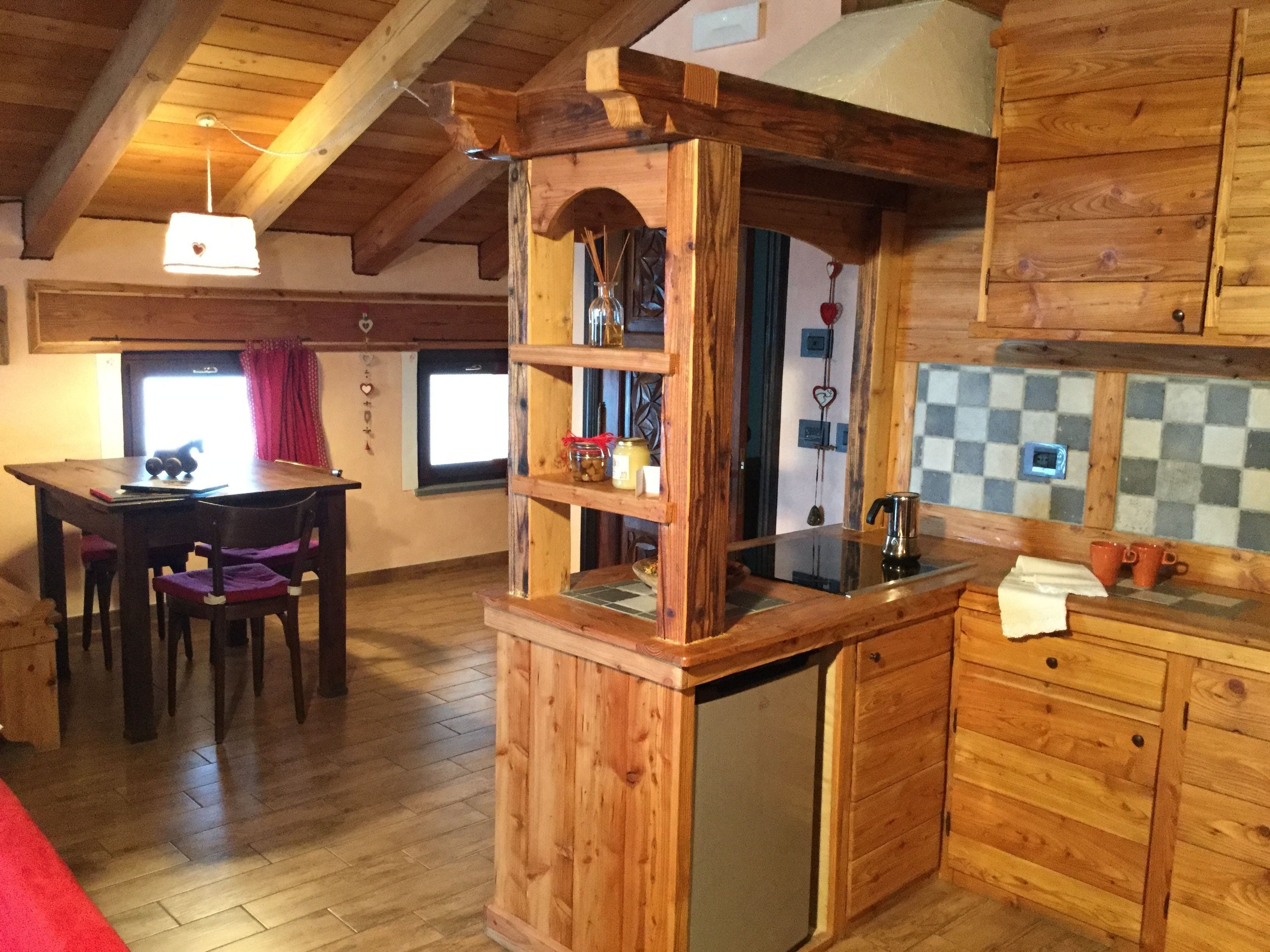 A wooden interior with a dining table, chairs, a kitchen area with a sink, and a refrigerator.