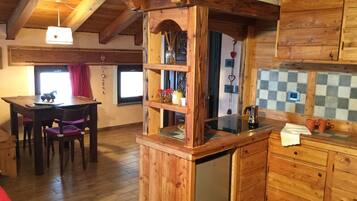 A wooden interior with a dining table, chairs, a kitchen area with a sink, and a refrigerator.