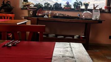 Un coin repas avec une table dressée pour deux personnes, une fenêtre donnant sur les montagnes et une étagère contenant divers objets.