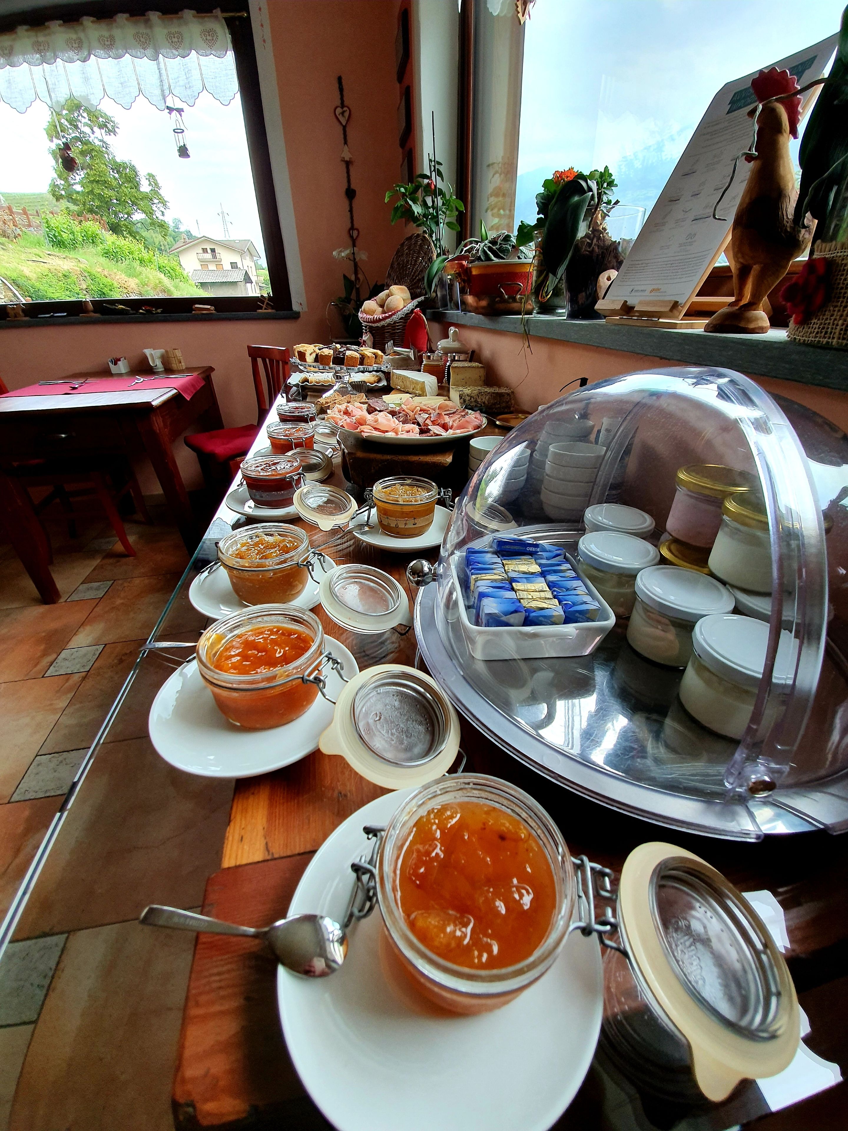 Una mesa de buffet con diversos alimentos y salsas, un expositor cubierto y vistas al exterior.