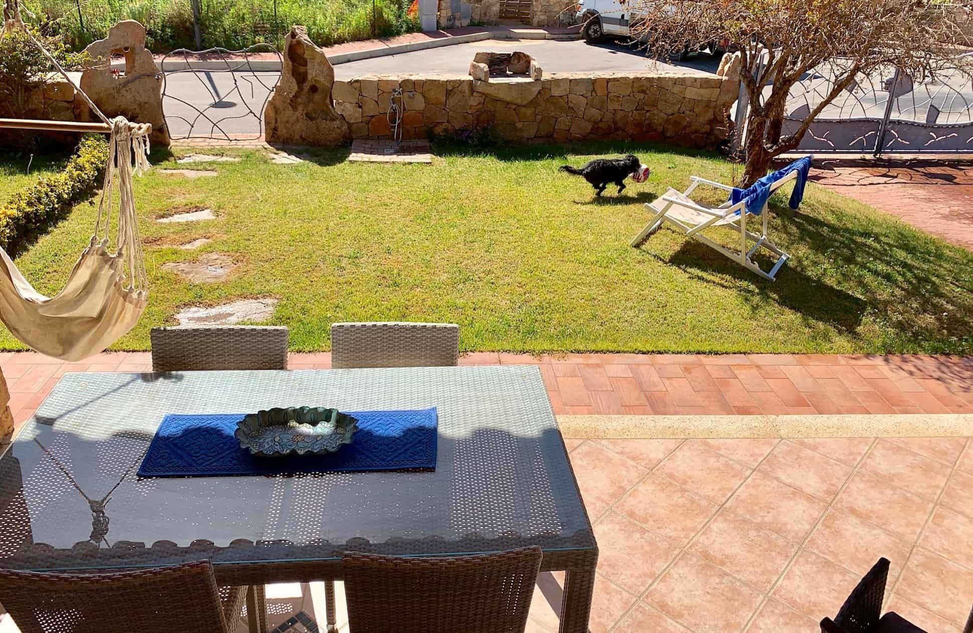 An outdoor patio with a table set for dining, a hammock, and a stone wall with a water feature.