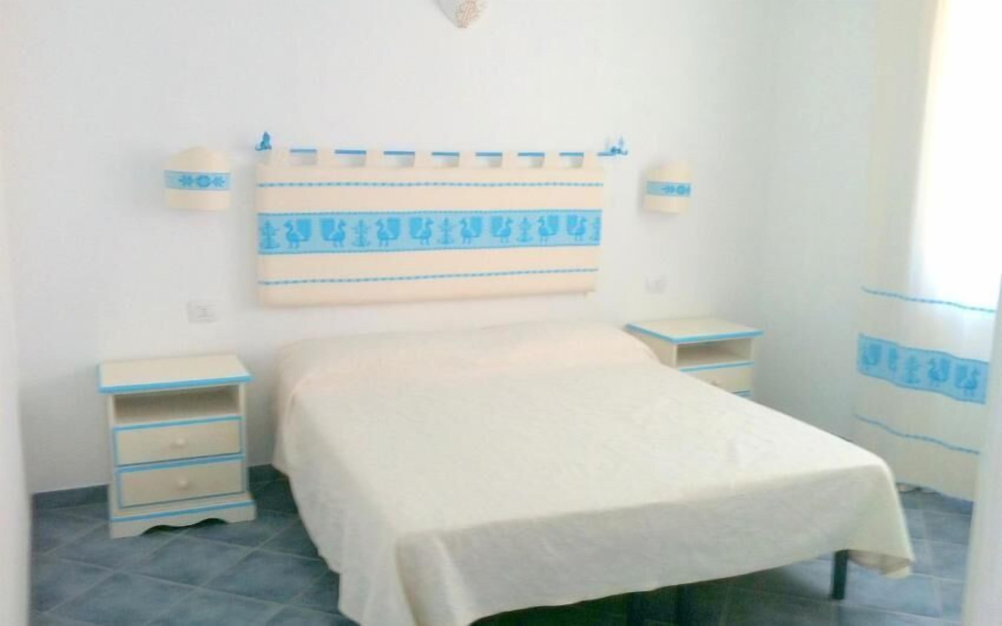 A bedroom with a bed, two bedside tables, and a wall-mounted shelf.