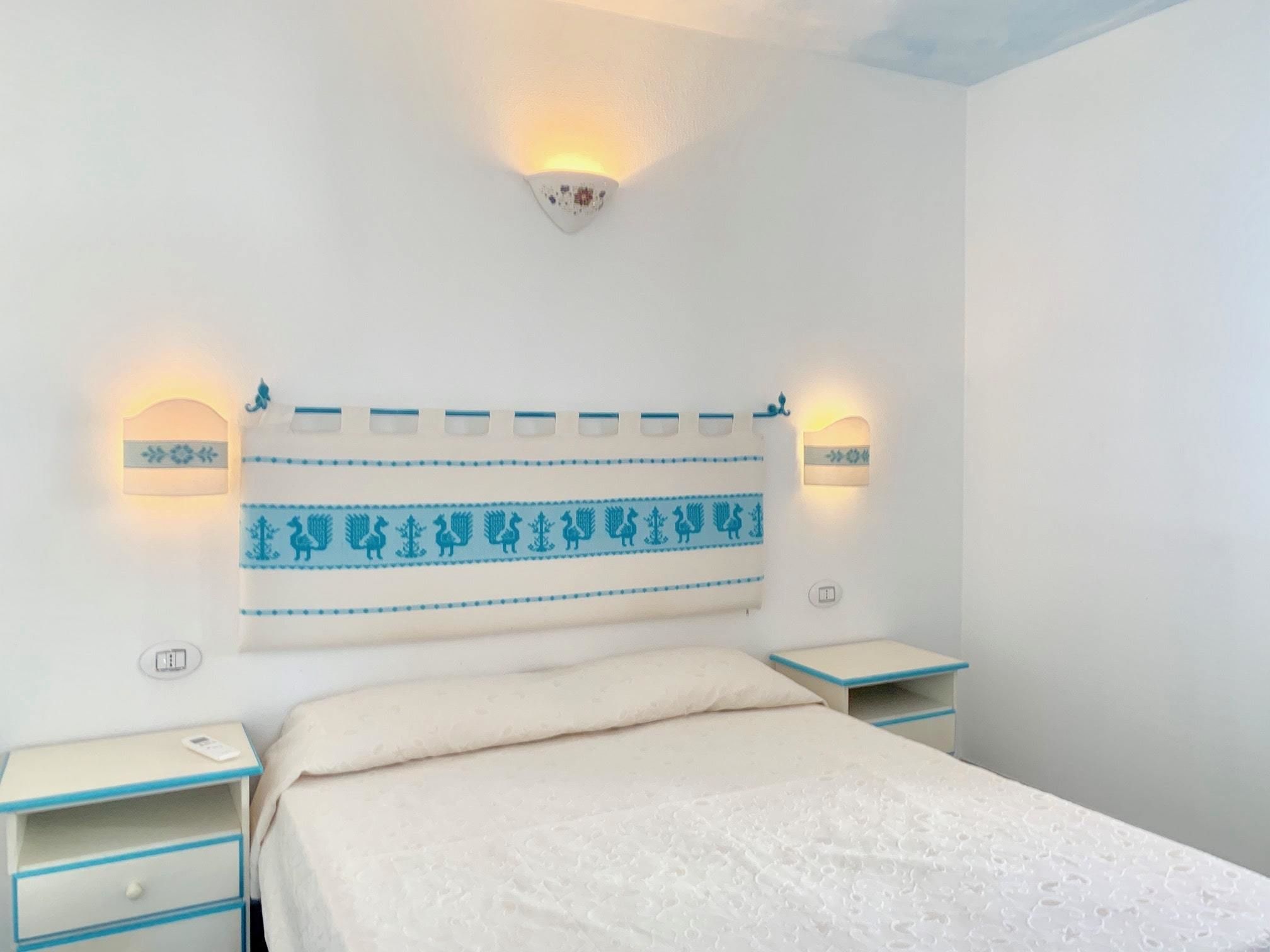 A bedroom with a bed, two bedside tables, and wall-mounted light fixtures.