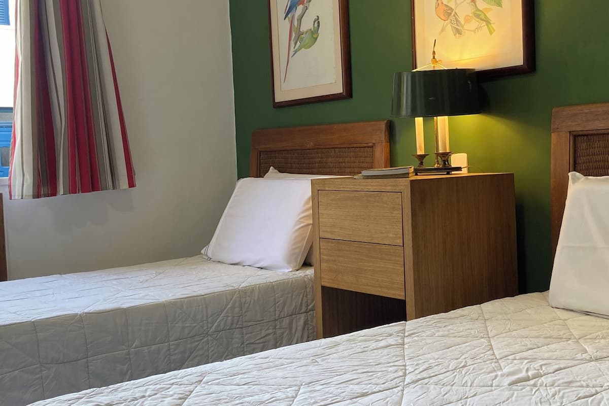 Habitación de hotel con dos camas, una mesita de noche con lámpara y dos cuadros enmarcados con pájaros en la pared.