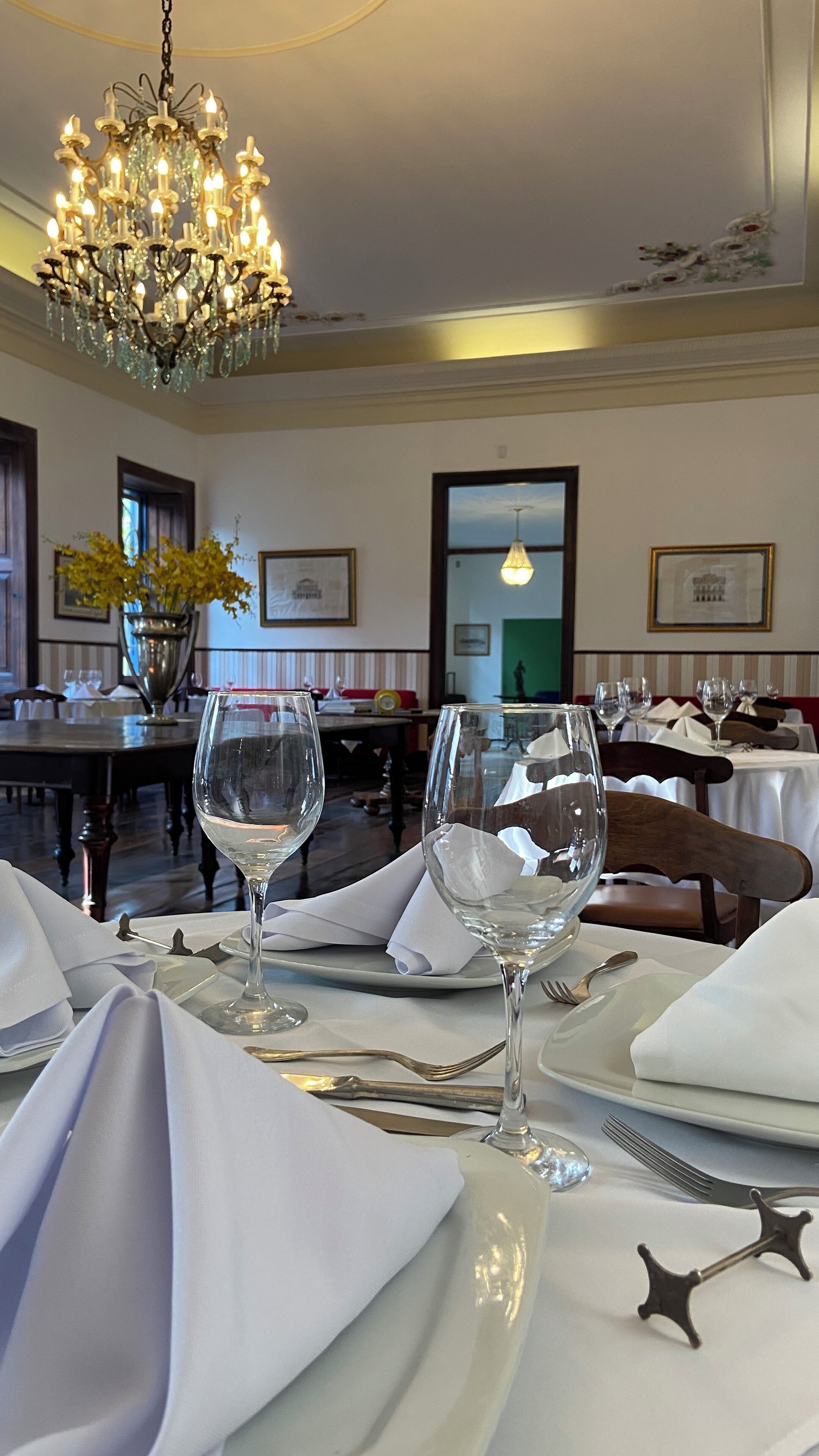 A dining area with tables set for a meal, a chandelier, and framed artwork on the walls.