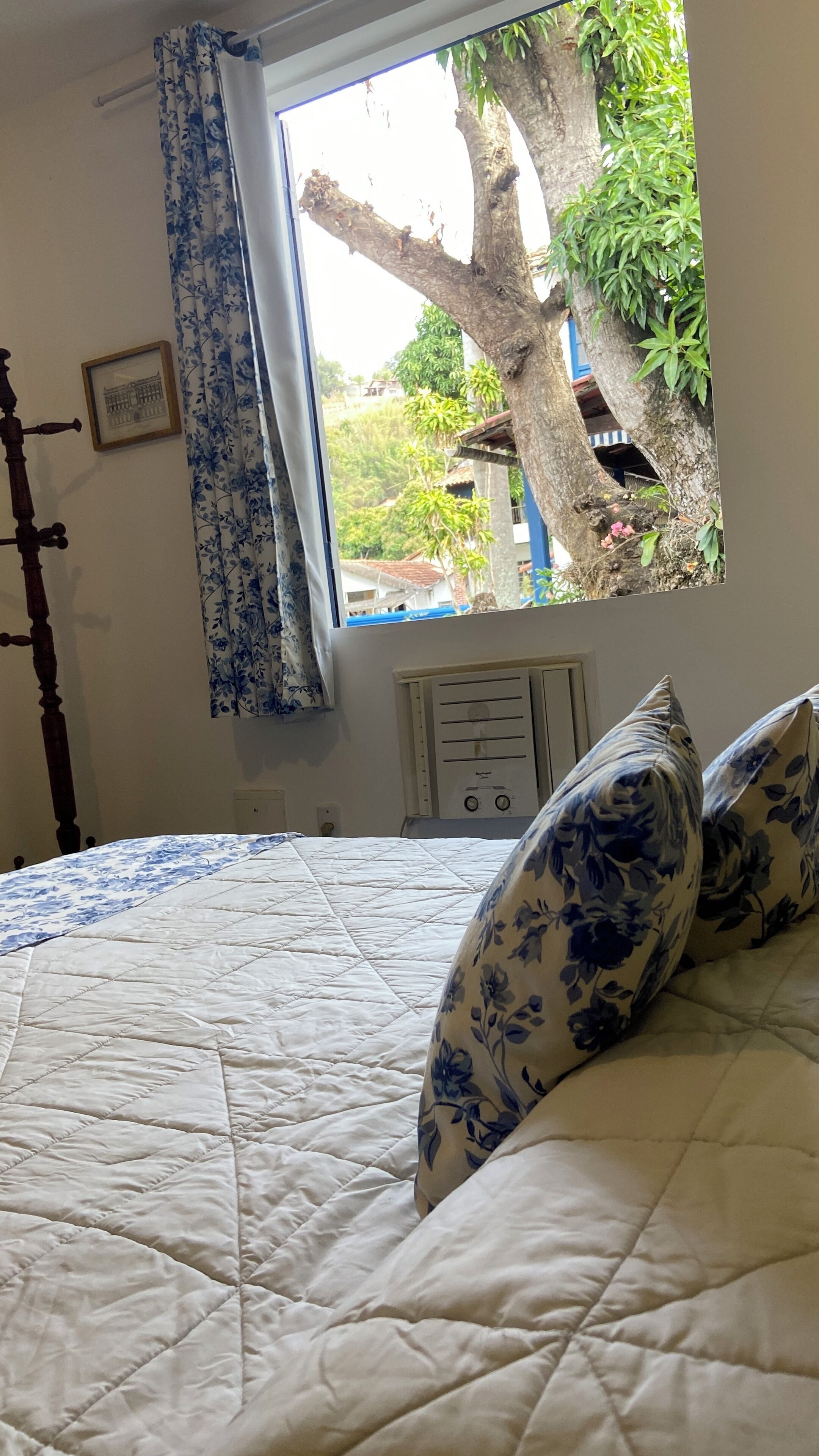 A bedroom with a large window, a bed with a quilted bedspread, and a wall-mounted heater.